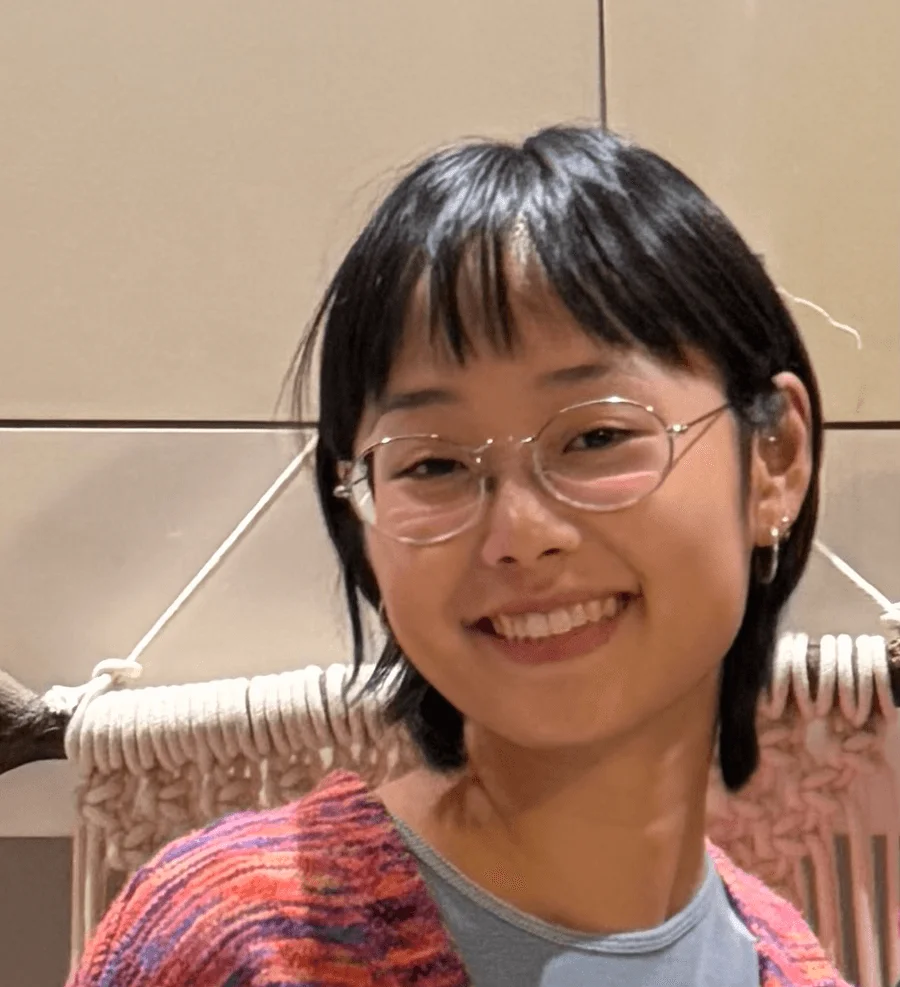 Paula Saizaki smiling, wearing glasses and a colorful cardigan.
